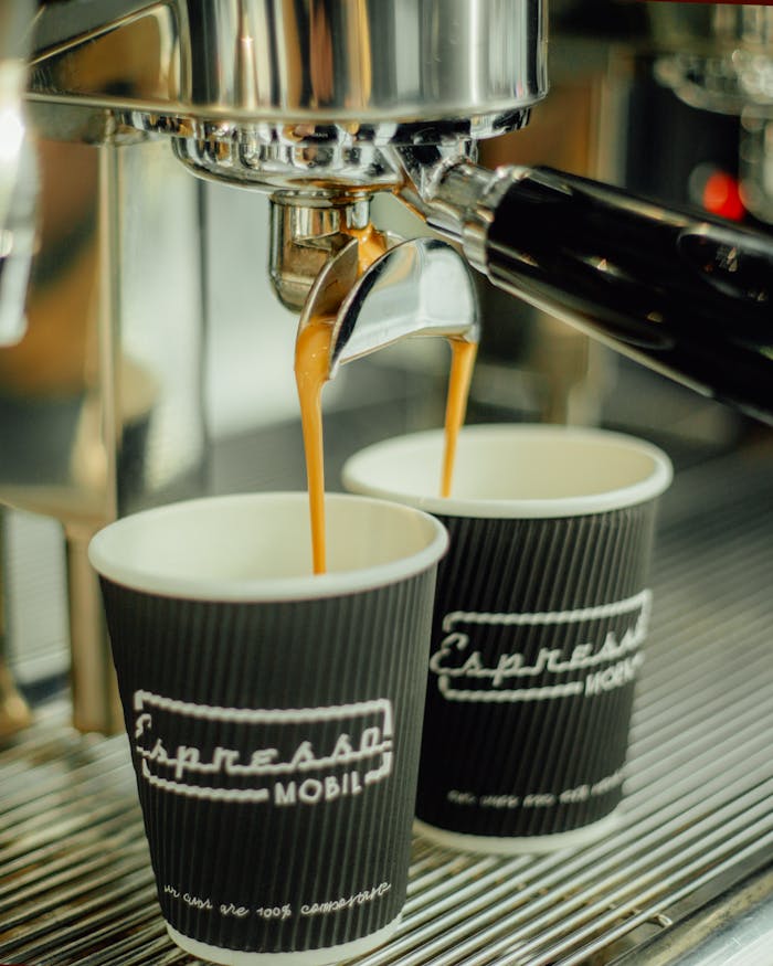 Espresso flows into paper cups from a coffee machine, perfect for coffee enthusiasts.